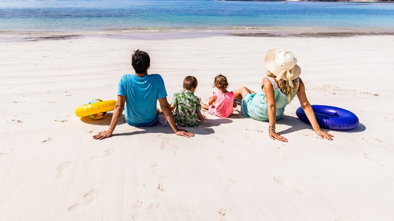 Panoramic view of a family from the back relaxing in sand on the beach and looking at view. Copy space.
