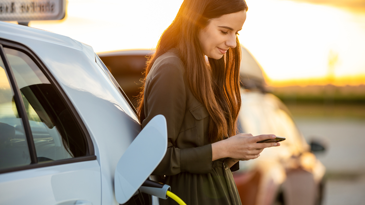 Femme chargeant une voiture électrique pendant qu’elle est au téléphone.